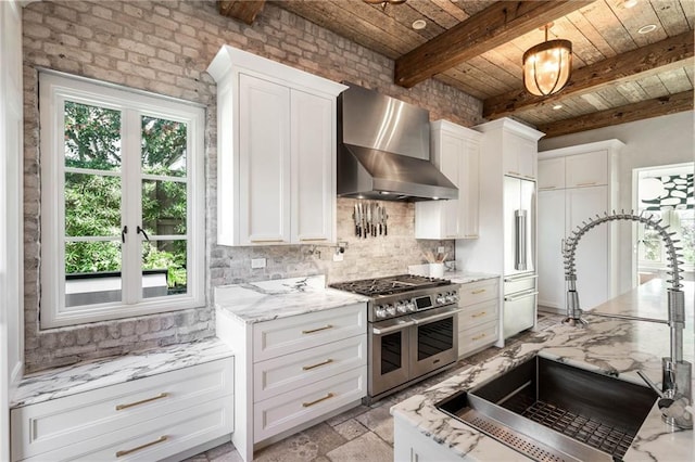 kitchen featuring beamed ceiling, white cabinetry, high quality appliances, and wall chimney range hood