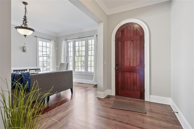 entrance foyer featuring baseboards, arched walkways, wood finished floors, and ornamental molding