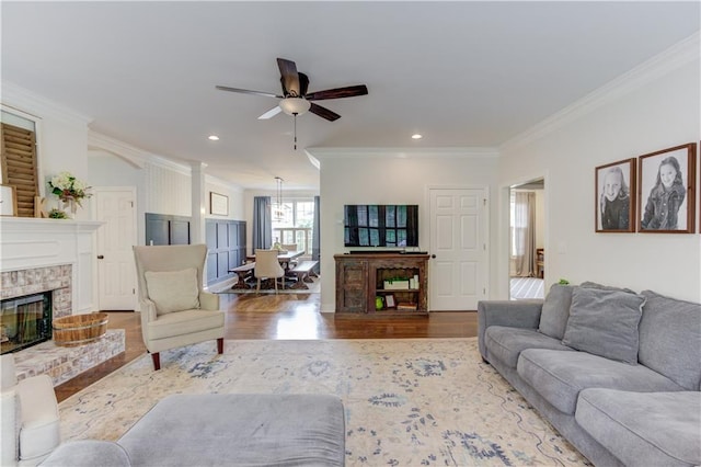 living room featuring crown molding, wood-type flooring, ceiling fan, and a brick fireplace