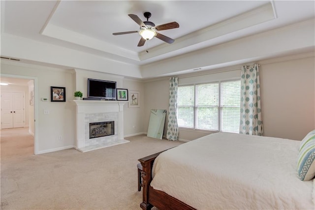 bedroom with a tile fireplace, light colored carpet, ceiling fan, and a tray ceiling