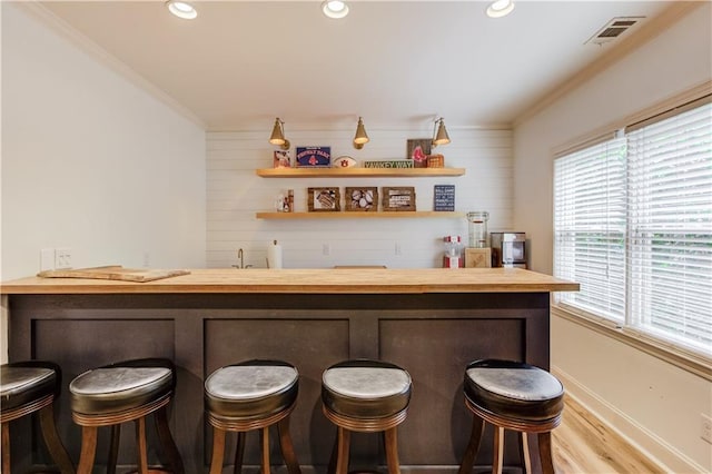 bar with wooden counters, ornamental molding, and light hardwood / wood-style floors