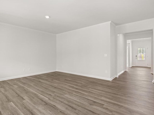 empty room with wood finished floors, crown molding, baseboards, and recessed lighting