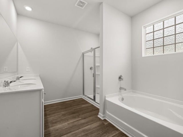 full bath featuring wood finished floors, a shower stall, a garden tub, double vanity, and baseboards