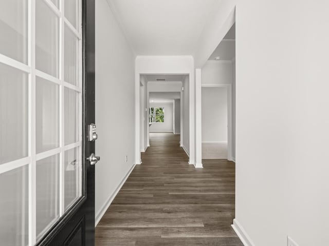 hall featuring dark wood-type flooring, crown molding, and baseboards