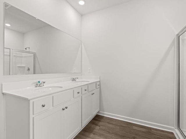 bathroom featuring wood finished floors, baseboards, a shower with door, double vanity, and recessed lighting