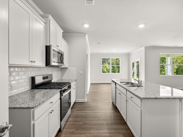 kitchen featuring appliances with stainless steel finishes, a sink, ornamental molding, a center island with sink, and white cabinetry