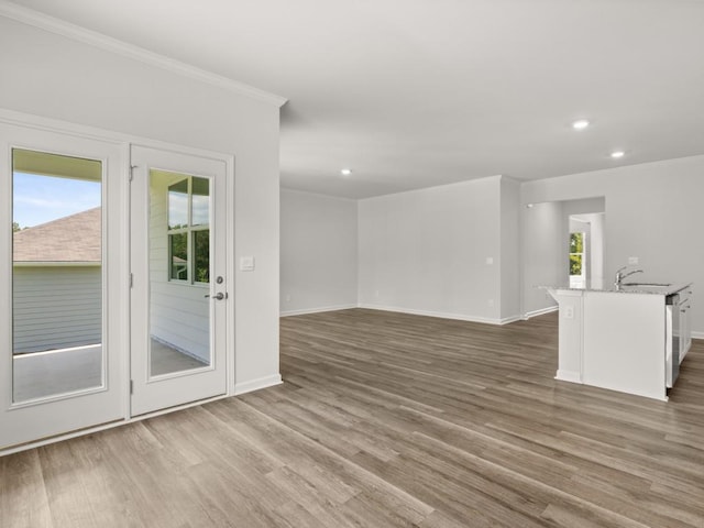 unfurnished living room featuring crown molding, recessed lighting, wood finished floors, baseboards, and a sink