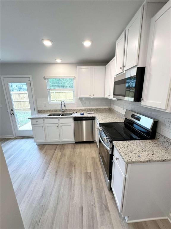 kitchen featuring appliances with stainless steel finishes, white cabinetry, light hardwood / wood-style floors, sink, and decorative backsplash