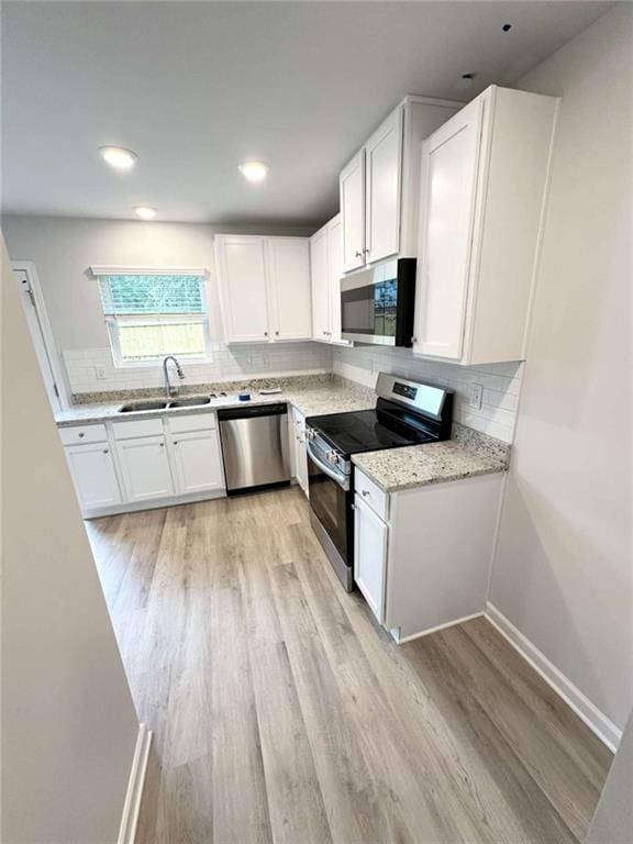 kitchen featuring white cabinetry, stainless steel appliances, light hardwood / wood-style floors, sink, and light stone counters