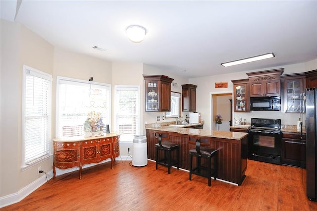4000 Longlake Dr, Duluth, GA 30097 - kitchen featuring black appliances, wood finished floors, a breakfast bar, and glass insert cabinets