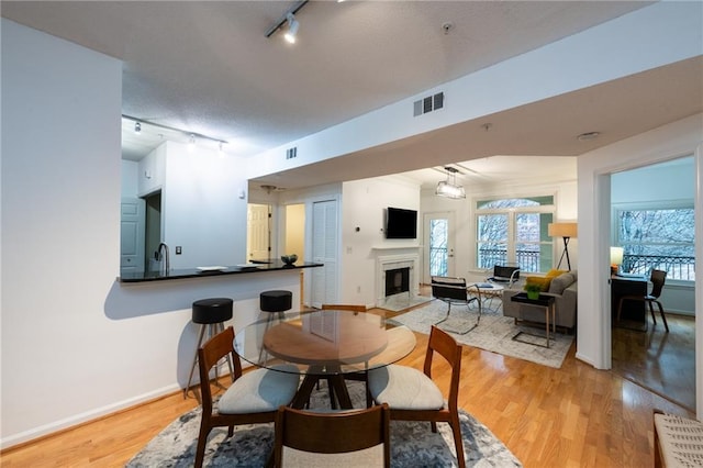 dining space with light wood finished floors, a fireplace with flush hearth, visible vents, and baseboards