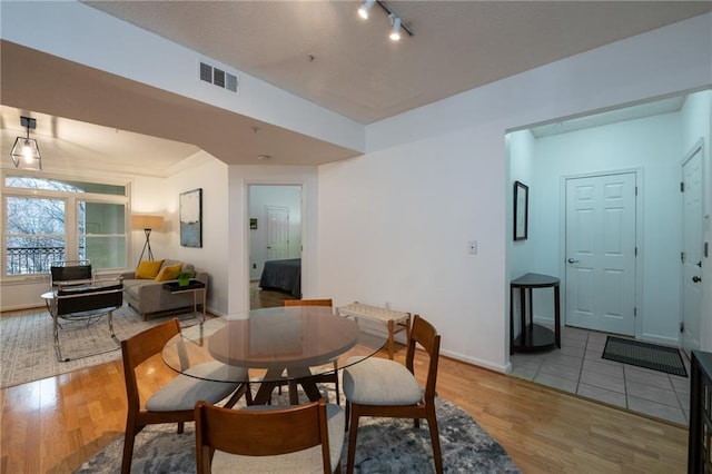 dining room with baseboards, track lighting, visible vents, and light wood-style floors