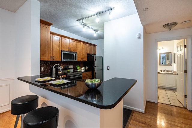 kitchen featuring stainless steel appliances, brown cabinetry, light wood-style floors, a peninsula, and a kitchen bar