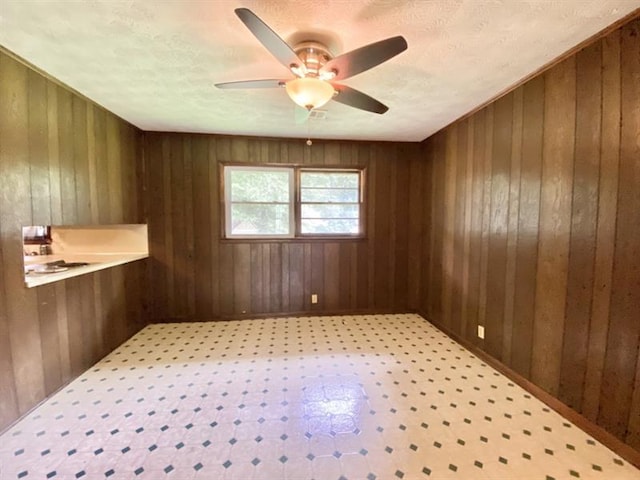 unfurnished room with a textured ceiling, light floors, wood walls, and a ceiling fan