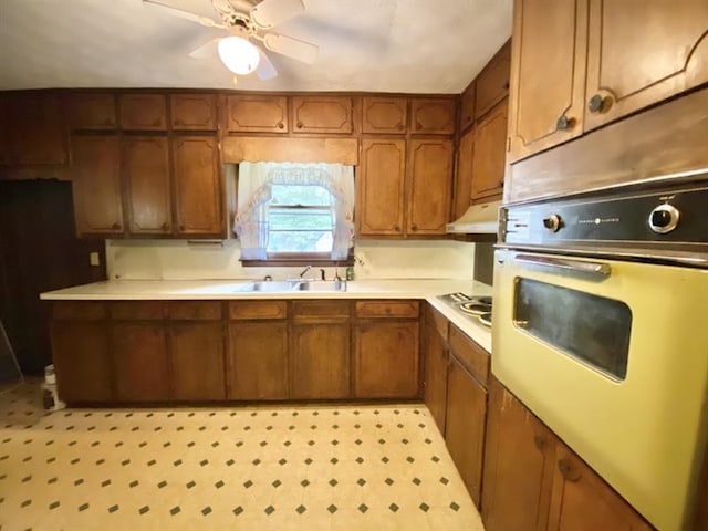 kitchen with wall oven, under cabinet range hood, light countertops, and brown cabinetry