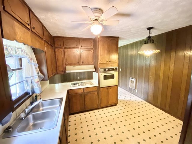 kitchen with white appliances, a sink, light countertops, brown cabinetry, and decorative light fixtures