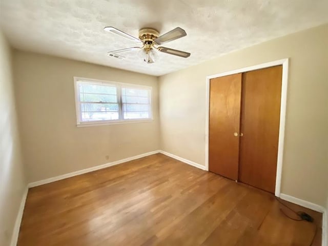 unfurnished bedroom with a textured ceiling, a closet, baseboards, and wood finished floors