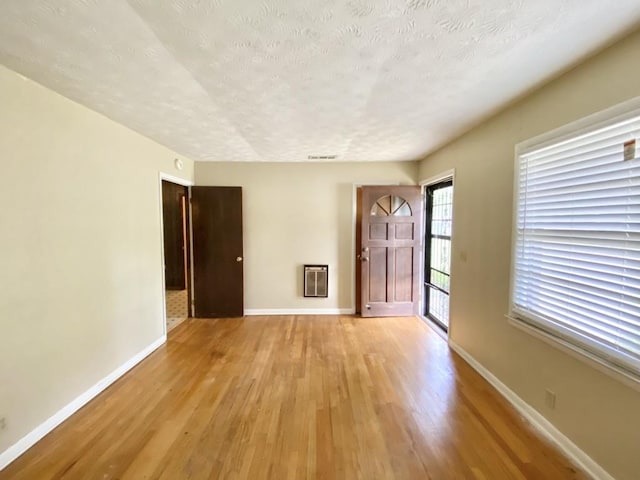 interior space featuring baseboards, light wood-style flooring, heating unit, and a textured ceiling