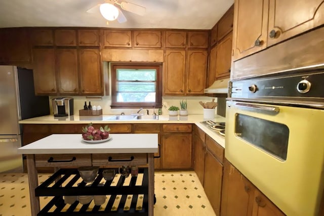 kitchen featuring brown cabinetry, light countertops, oven, and under cabinet range hood