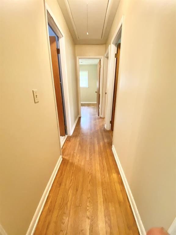 hall with light wood-type flooring, attic access, and baseboards