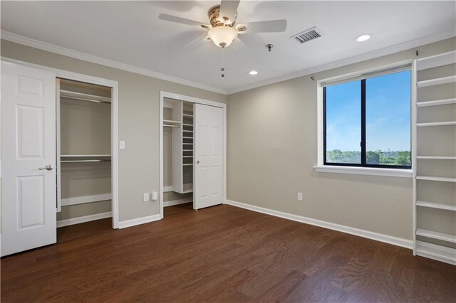 unfurnished bedroom with ceiling fan, crown molding, dark hardwood / wood-style floors, and multiple closets