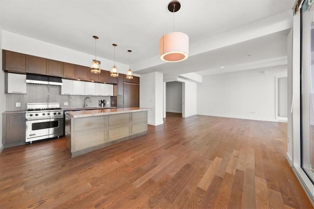 kitchen with pendant lighting, backsplash, light stone counters, high end stove, and a kitchen island