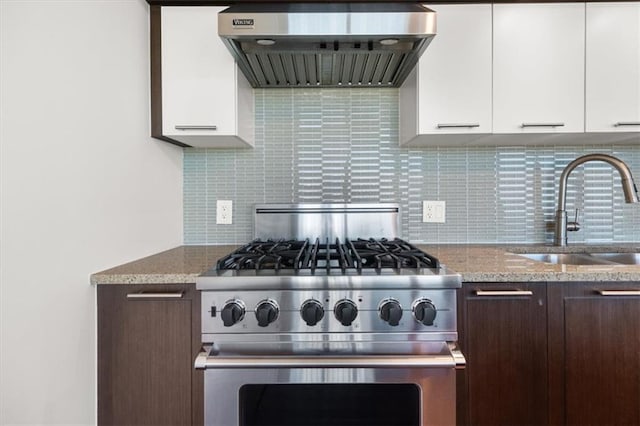 kitchen featuring sink, wall chimney range hood, stainless steel stove, white cabinets, and decorative backsplash