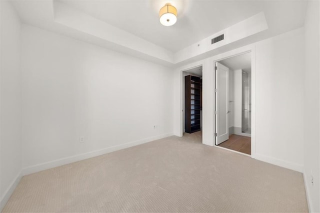 unfurnished bedroom featuring a tray ceiling and light colored carpet