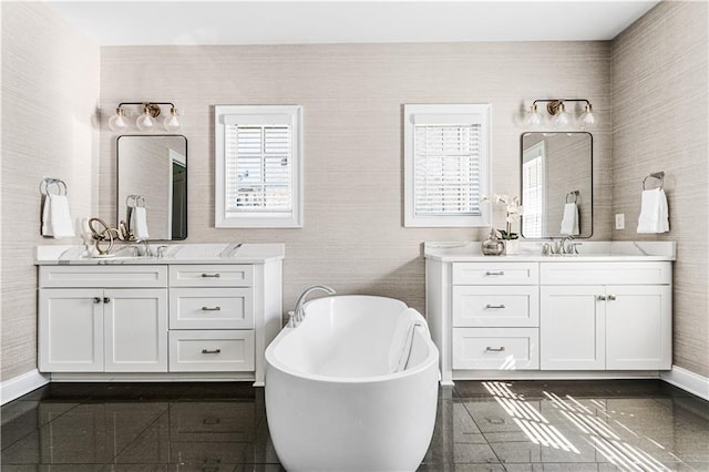 full bath with a sink, granite finish floor, a freestanding bath, and two vanities