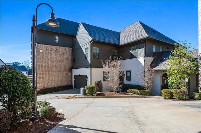 view of front of house featuring a garage, concrete driveway, brick siding, and a high end roof