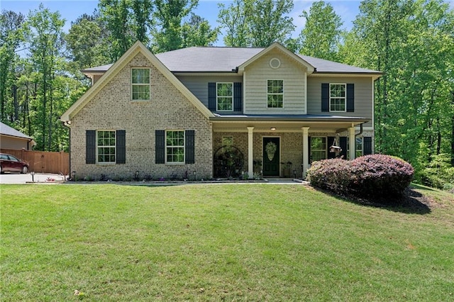 view of front of home featuring covered porch, brick siding, fence, and a front lawn