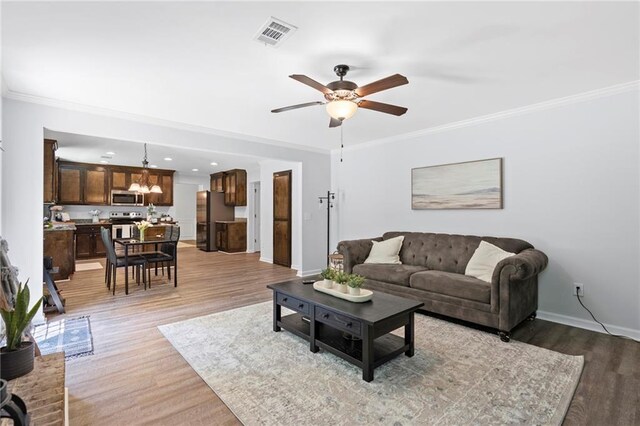 living room with visible vents, baseboards, ceiling fan with notable chandelier, light wood-style floors, and ornamental molding