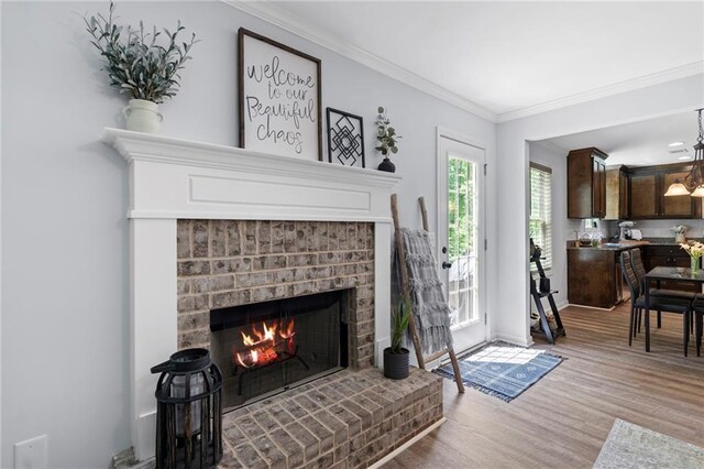 living area featuring a brick fireplace, crown molding, baseboards, and wood finished floors