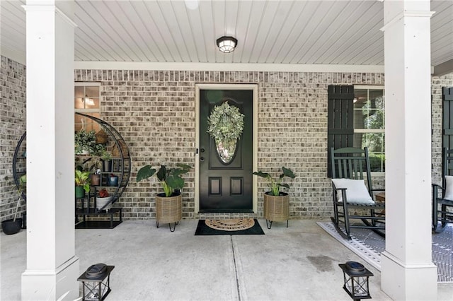 doorway to property with a porch and brick siding
