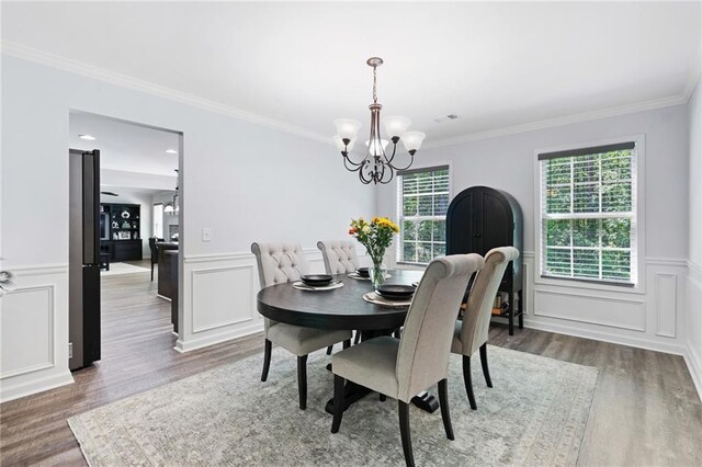 dining space featuring crown molding, a decorative wall, wood finished floors, and a chandelier