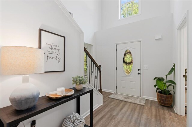 entryway with stairway, plenty of natural light, wood finished floors, and a towering ceiling