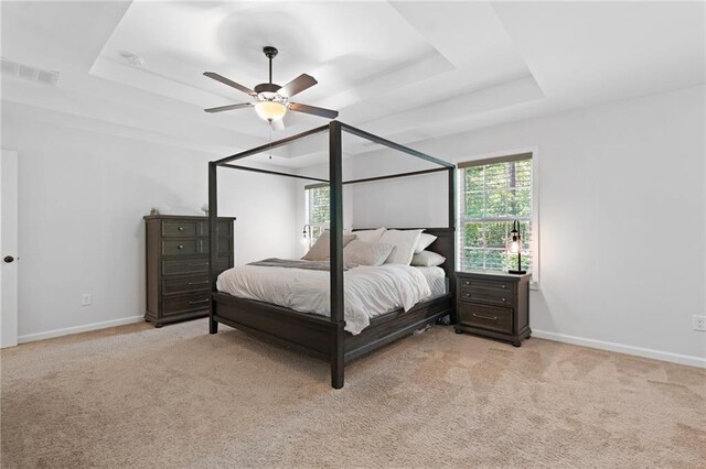 bedroom with multiple windows, light carpet, a tray ceiling, and visible vents