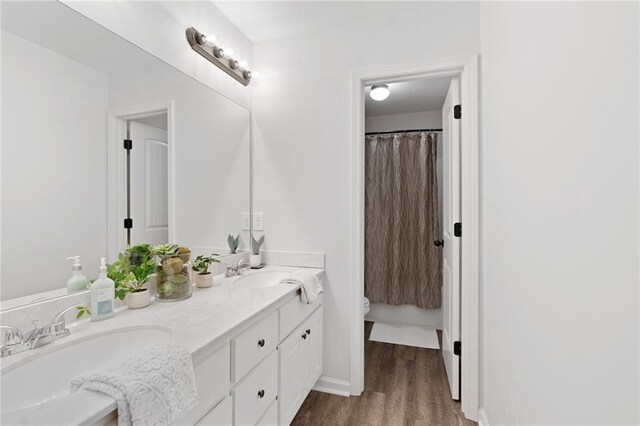 full bath featuring a sink, double vanity, toilet, and wood finished floors