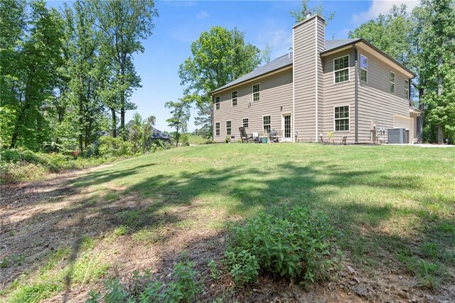 rear view of house featuring a lawn, a garage, central AC, and a chimney