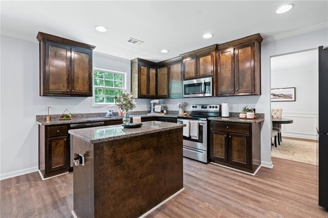 kitchen with dark brown cabinetry, appliances with stainless steel finishes, light wood-type flooring, visible vents, and ornamental molding
