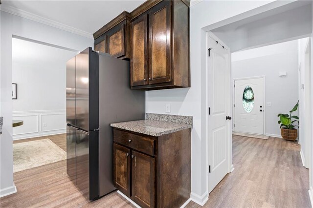 kitchen featuring light wood-style floors, ornamental molding, dark brown cabinetry, and light stone countertops