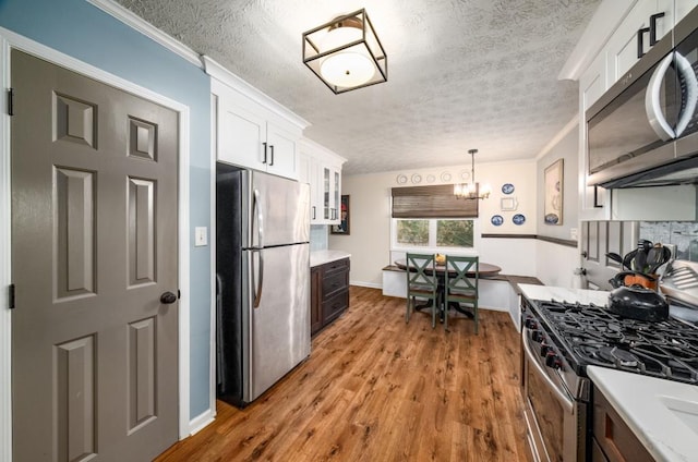 kitchen featuring stainless steel appliances, white cabinets, an inviting chandelier, decorative light fixtures, and ornamental molding