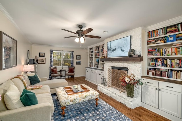 living room featuring hardwood / wood-style floors, ceiling fan, crown molding, and a stone fireplace