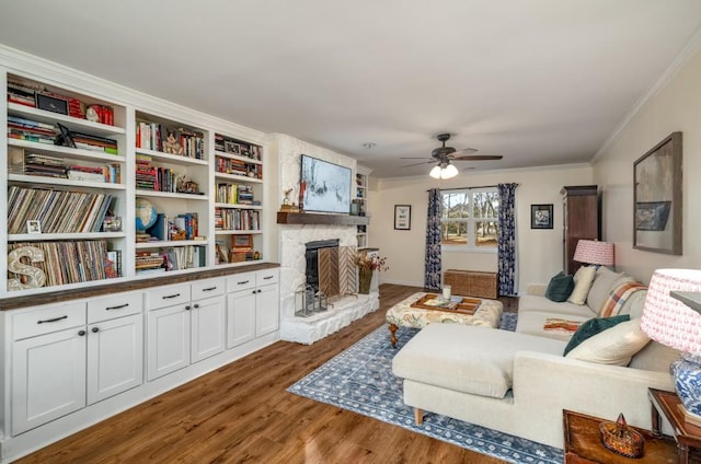 living room featuring ceiling fan, dark hardwood / wood-style flooring, a stone fireplace, and crown molding