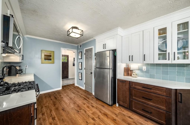 kitchen featuring wood-type flooring, stainless steel appliances, crown molding, white cabinetry, and backsplash