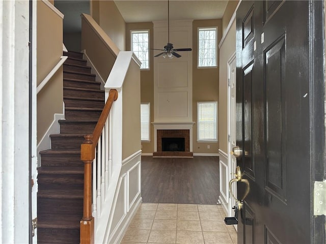 tiled foyer featuring baseboards, stairs, a fireplace, a towering ceiling, and a ceiling fan