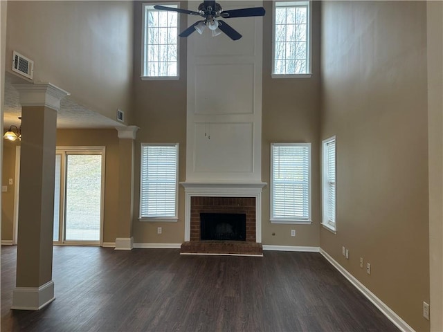 unfurnished living room with visible vents, baseboards, dark wood finished floors, decorative columns, and a fireplace