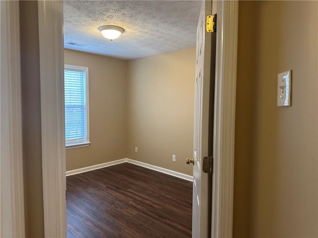 spare room featuring visible vents, a textured ceiling, dark wood-type flooring, and baseboards