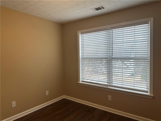 empty room with dark wood-type flooring, baseboards, visible vents, and a textured ceiling