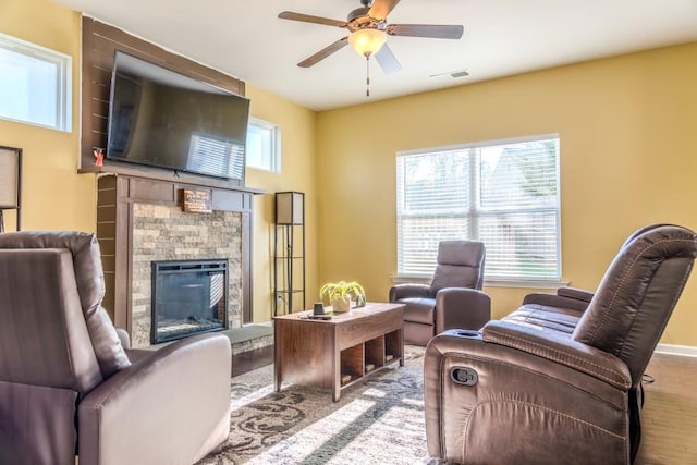 living room with ceiling fan, light hardwood / wood-style floors, and a stone fireplace